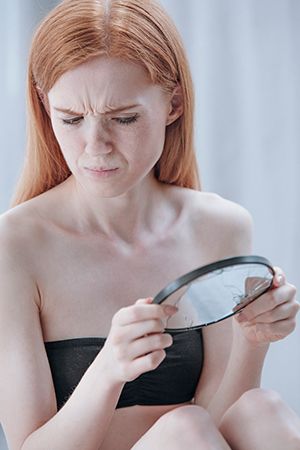 mujer mirándose en un espejo pequeño con el ceño fruncido