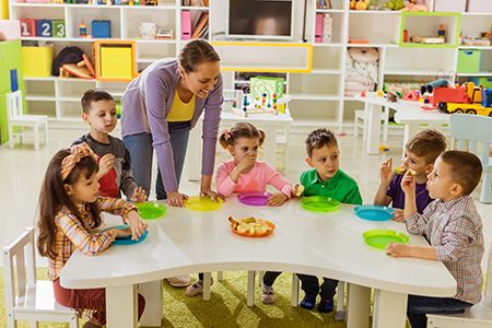 profesora enseñando a comer a niños en el colegio