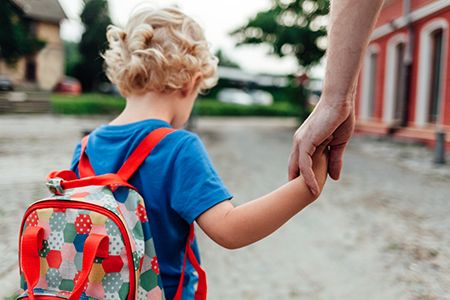 niños de espaldas con mochila de la mano de persona mayor