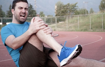 hombre deportista con gesto de dolor agarrándose la rodilla