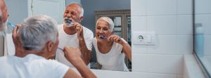 pareja de personas mayores lavándose los dientes enfrente de un espeo