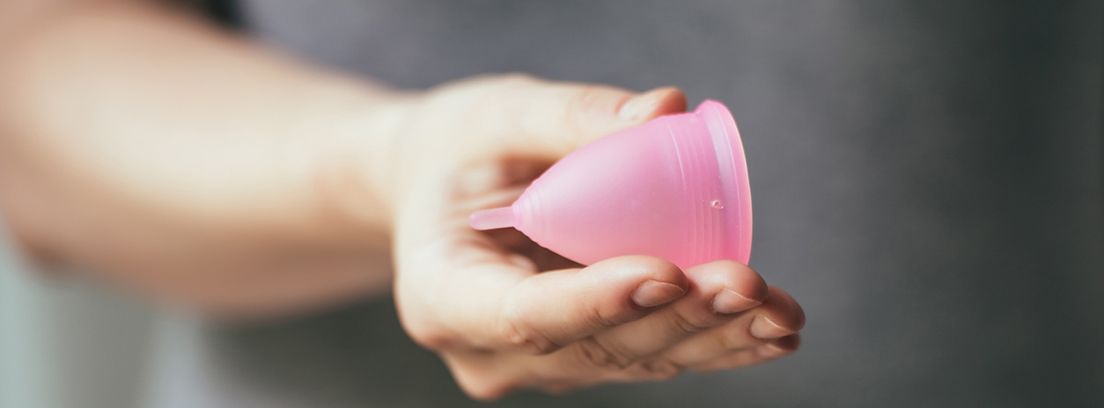 mano sujetando una copa menstrual de color rosa