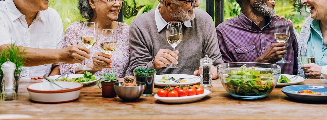 personas mayores con una copa de vino en la mano en una mesa con comida