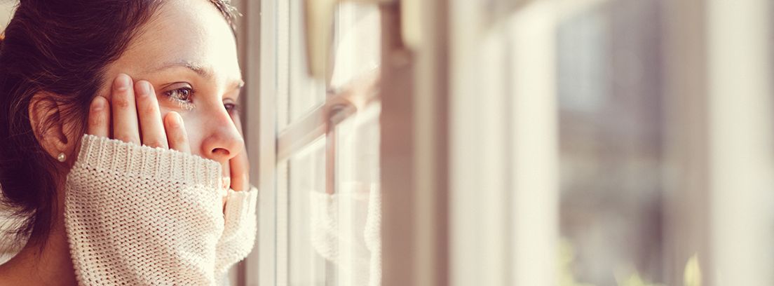 mujer mirando por la ventana con las manos sobre el rostro