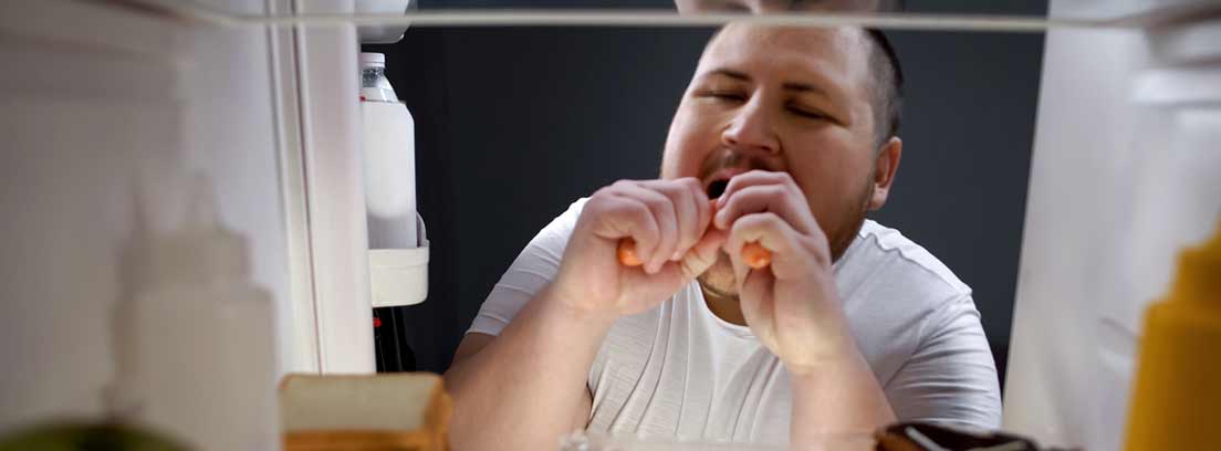 hombre comiendo salchichas con la nevera abierta