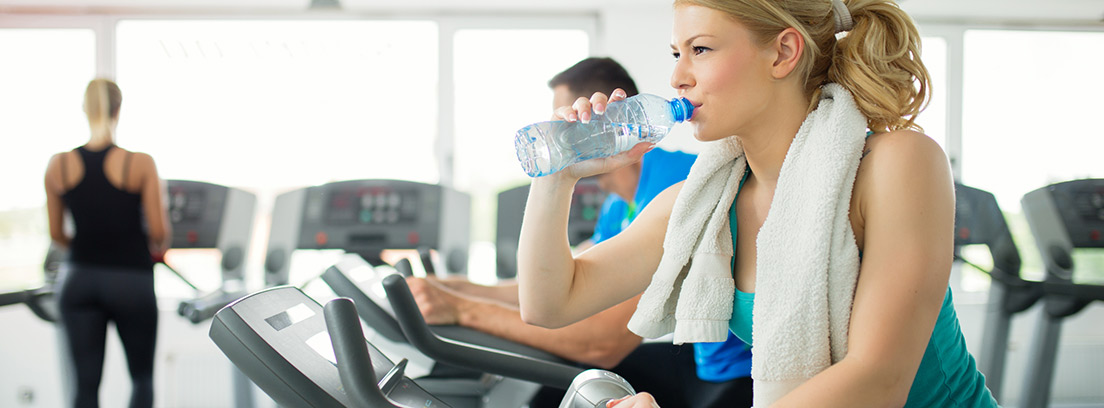 mujer deportista en cinta de correr bebiendo agua en una botella