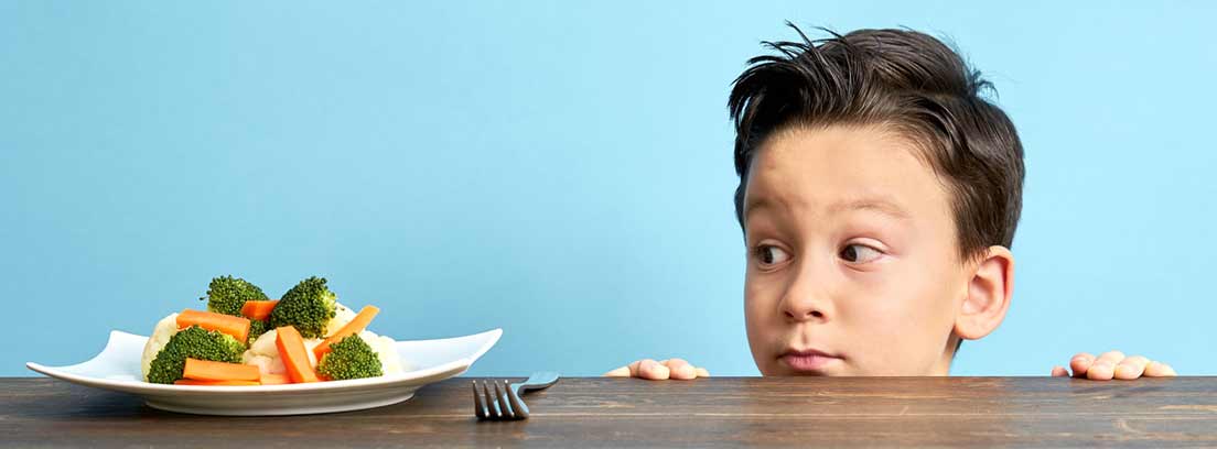 niño mirando por encima de la mesa un plato con verduras