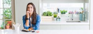 Chica con la mano en la boca con un plato de sushi en la encimaera de la cocina