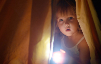 niña detrás de una cortina con una linterna en la mano