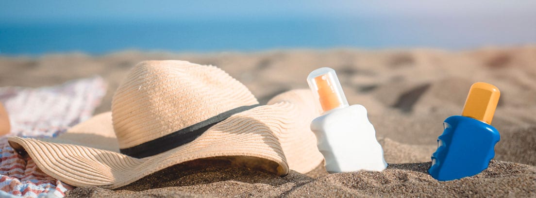 Prtector solar en la infancia: sobrero y varios protectores solares en la arena de la playa