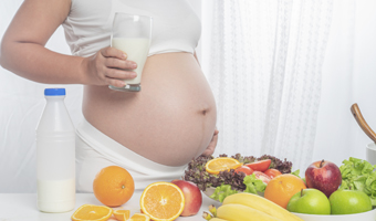Mujer embarazada con un vaso de leche y fruta