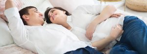 mujer embarazada conb las manos cubriéndole la tripa y hombre tumbados en una cama