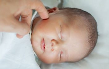 bebé durmiendo y una mano rozándole la cara