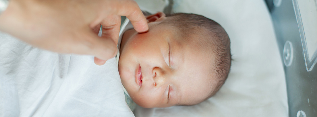 bebé durmiendo y una mano rozándole la cara