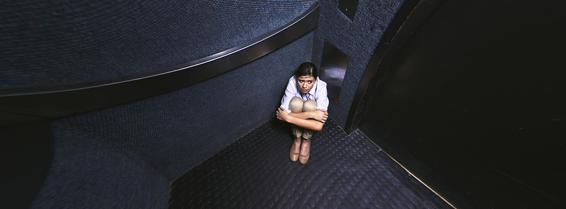 chica sentada en el suelo en un rincón del ascensor 