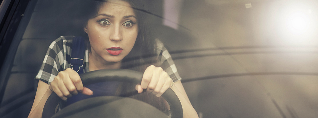 mujer joven al volante con gesto asustado
