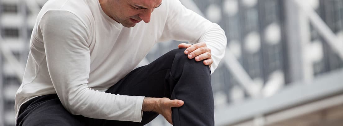 Lesión músculos isquiotibiales: hombre sentado en unas escaleras con un tirón en la pierna