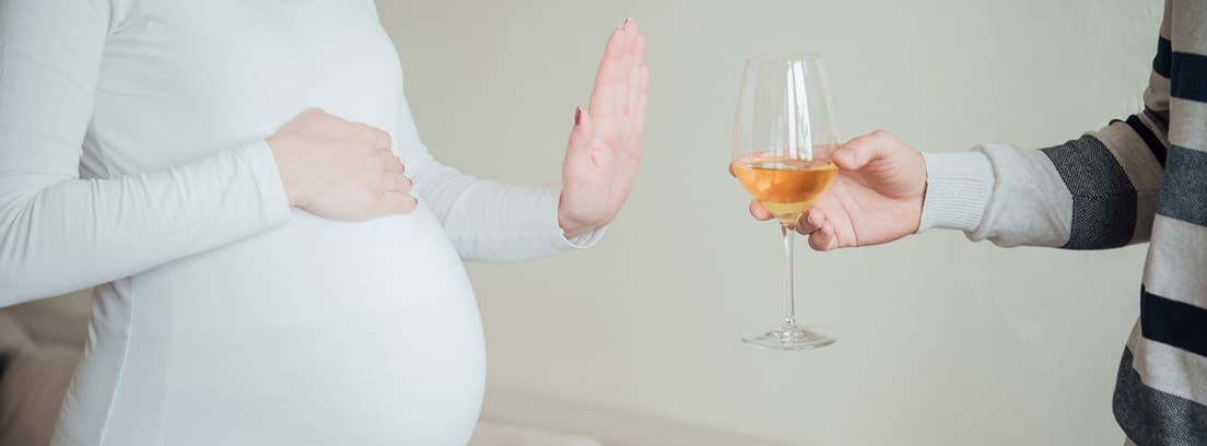 Mujer embarazada negando con la mano una copa de alcohol