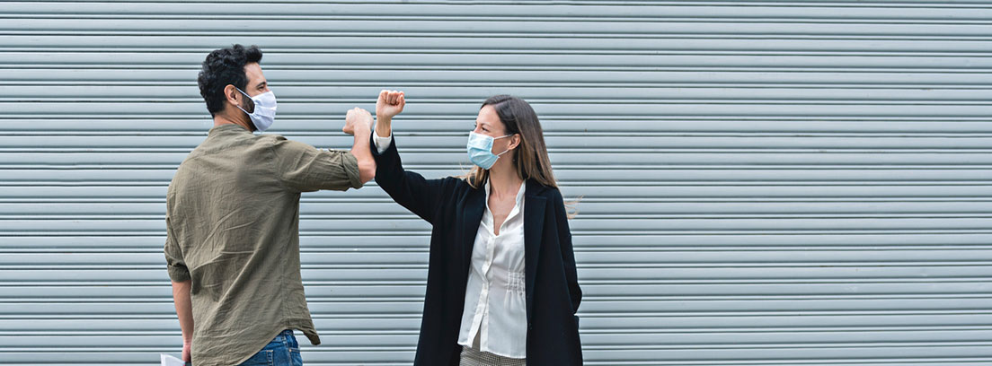 ¿Cómo afecta la nueva normalidad a nuestra salud? : chico y chica con mascarillas saludándose con los codos