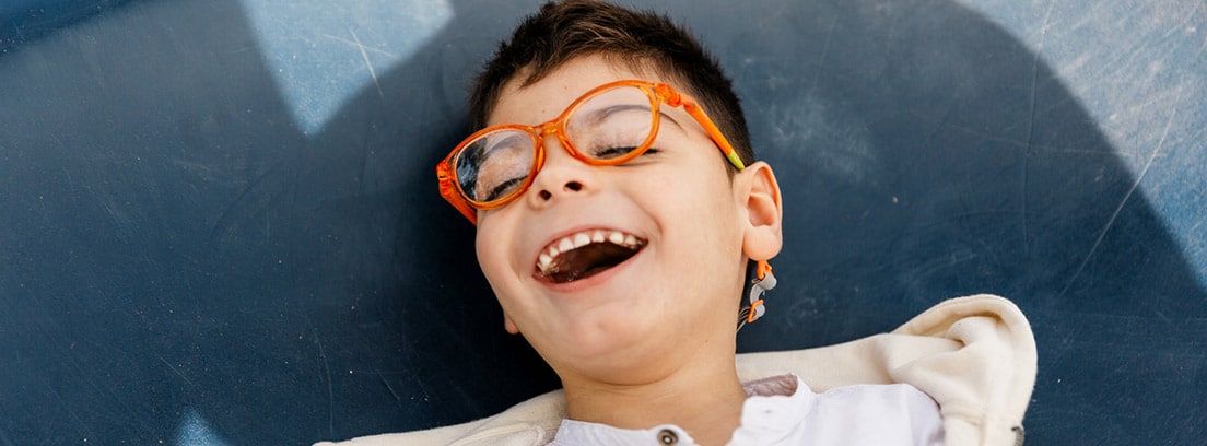 Enfermedad de Leigh: niño riéndose con unas gafas naranjas