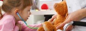Enfermedad de Leigh: La mano niña con un estetoscopio escuchando el corazón de un oso de peluche en consulta médica