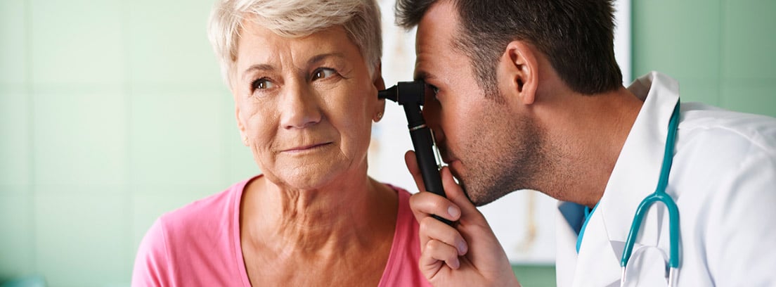 Eliminar los tapones de cera de los oídos:Otorrino revisando el oído de una mujer mayor