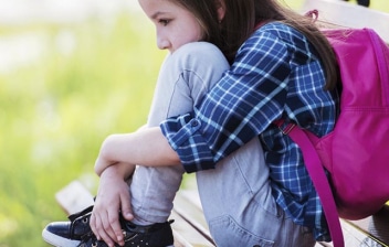 Qué significa tener un retraso madurativo: niña sentada con los brazos rodeando las rodillas y una mochila en la espalda