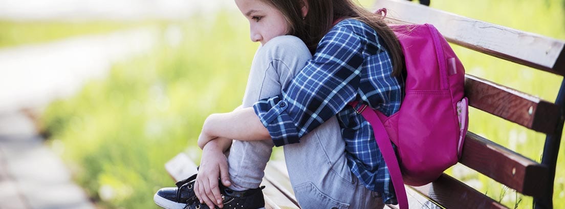 Qué significa tener un retraso madurativo: niña sentada con los brazos rodeando las rodillas y una mochila en la espalda
