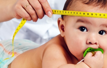 ¿Qué es la macrocefalia?: bebé tumbado boca abajo y médico midiéndole el perímetro cefálico