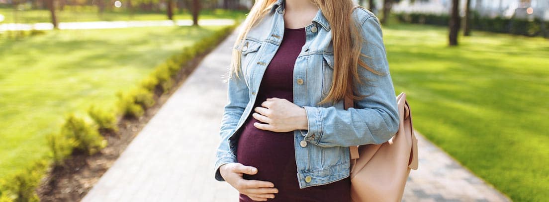 Mujer embarazada paseando por un parque sosteniendose la tripa