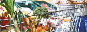 Consejos para hacer una compra saludable: mujer con un carrito de compra en supermercado lleno de verdura y frutas