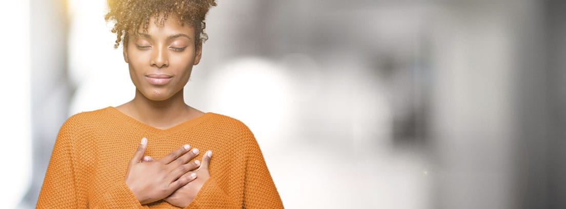 Personas altamente sensibles: chcia joven con sueter naranja, los ojos cerrados y la mano en el pecho