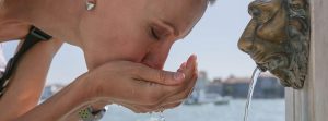 Es bueno beber 2 o 3 litros de agua al día para la salud: mujer bebiendo agua en las manos de una fuente