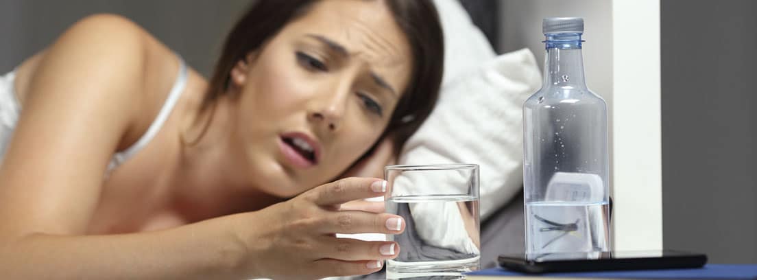 Beber agua: mujer en la cama cogiendo un vaso de agua