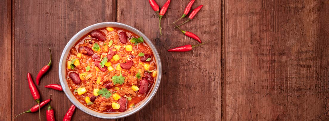 Picante, beneficios y contraindicaciones: plato de comida picante con chiles alrededor sobre una mesa de madera