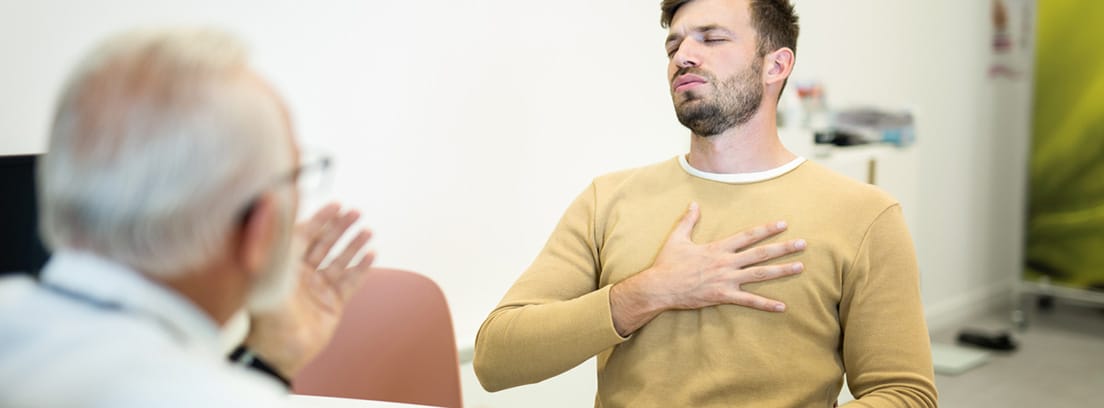 Dolor torácico: chico joven en consulta de médico con la mano puesta en el tórax en señal de dolor