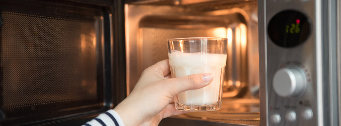 Cocinar con microondas: mano metiendo un vaso de leche en un microondas