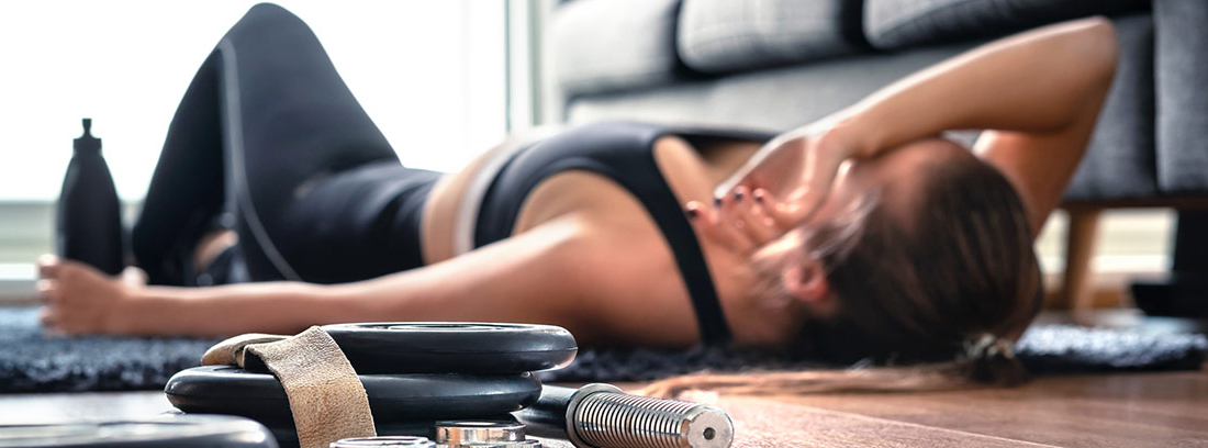 Desventajas de practicar ejercicio con exceso: mujer deportista tumbada en el suelo con fatiga