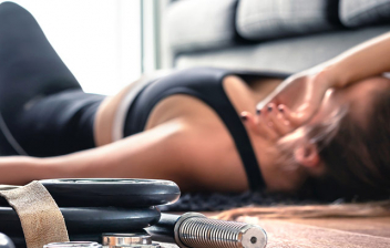 Desventajas de practicar ejercicio con exceso: mujer deportista tumbada en el suelo con fatiga
