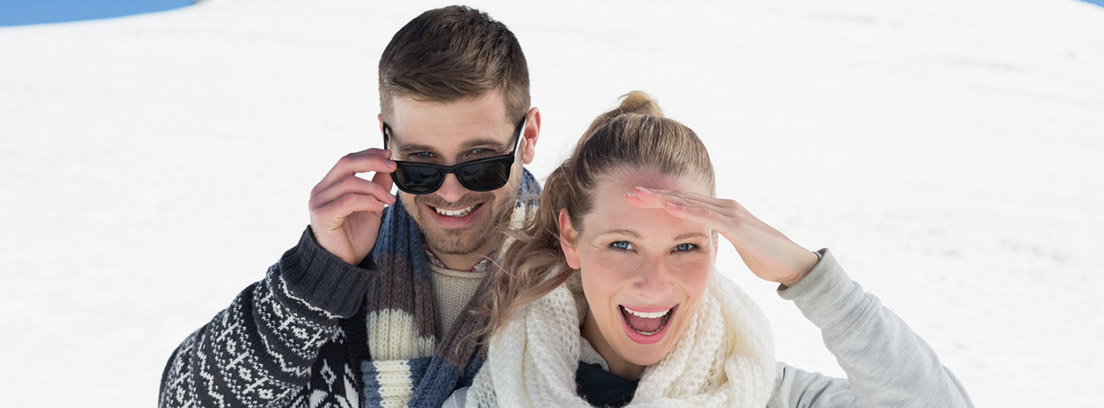 Fotoqueratitis: pareja de jóvenes en la nieve protegiéndose con gafas de sol