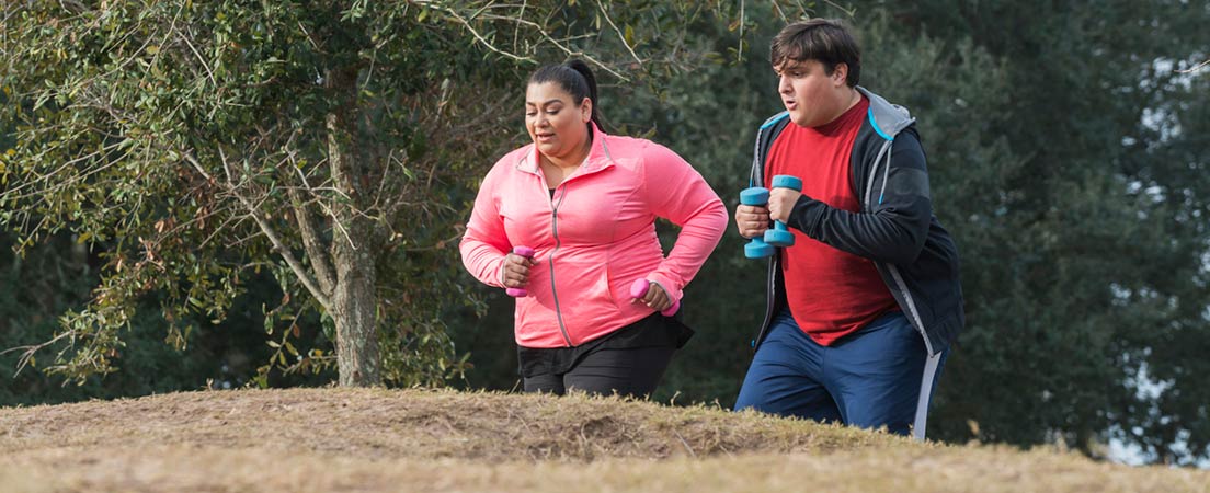 Estudio científico que confirma la necesidad del ejercicio para perder grasa: Un hombre y una mujer con exceso de peso realizando ejercicio por el campo