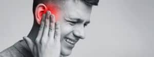 Causas y tratamiento para el dolor de oídos:chico joven con la mano en el oído, con síntomas de dolor