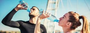 Bebidas deportivas: chico y chica bebiendo agua después de hacer ejercicioi