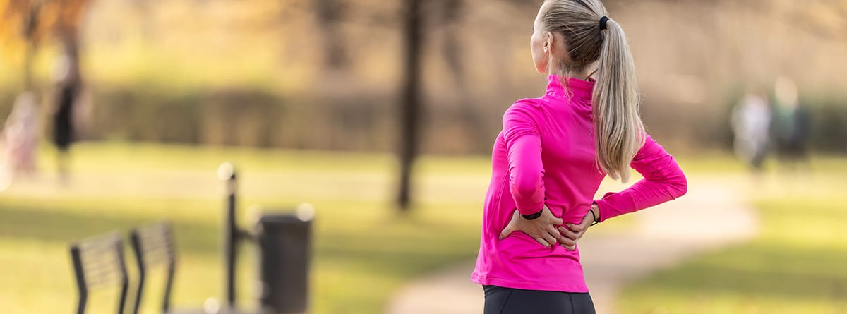 Prevenior dolor de espalda en el corredor: mujer deportista con las manos en la espalda con síntoma de dolor