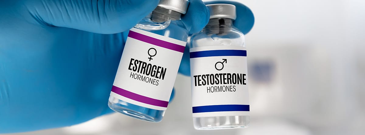 Estradiol: Mano del médico con dos viales de inyección para el tratamiento con hormonas testosterona y estrógeno.