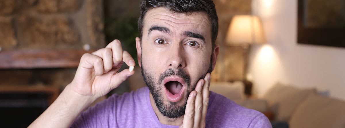 Edentulismo cuando se caen los dientes: hombre joven con la boca abierta y un diente en la mano