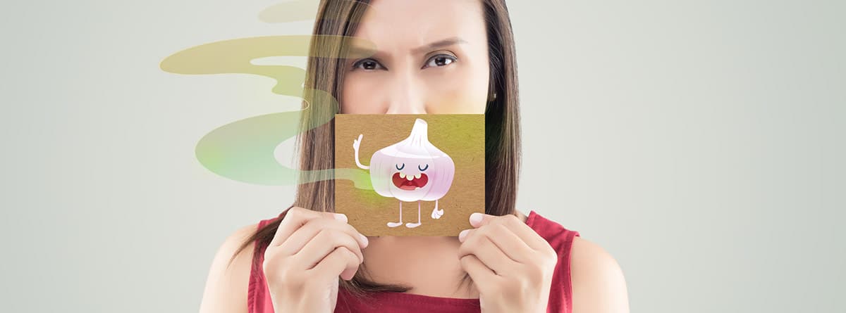 Prevenir la halitosis: mujer con camiseta roja sosteniendo un papel sobre su boca y con el dibujo de un ajo. 