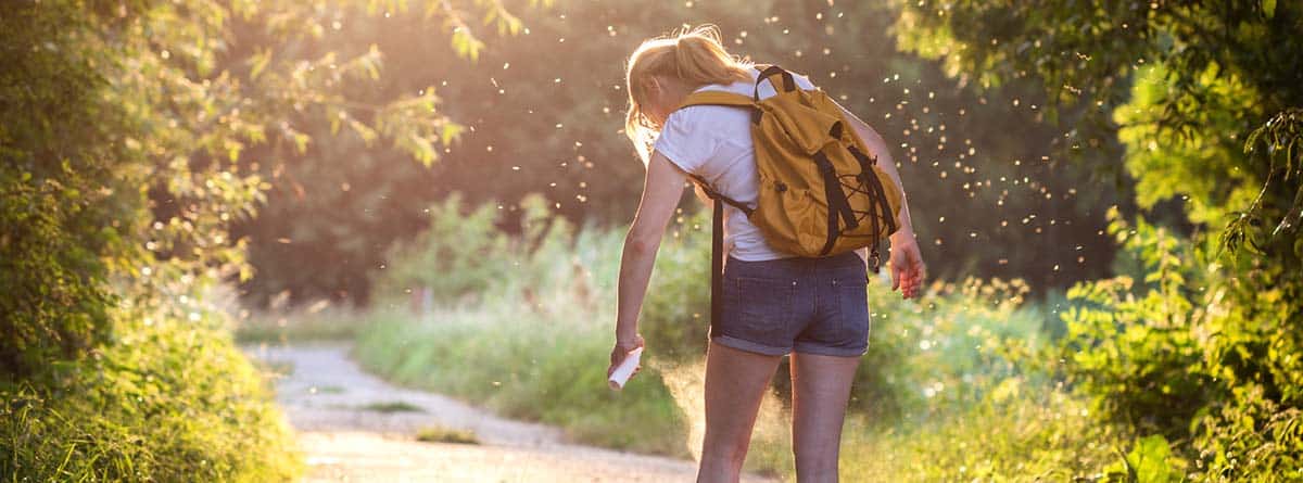 Los males del verano: chica joven en el campo con mosquitos a su alrededor y rociándose de spray