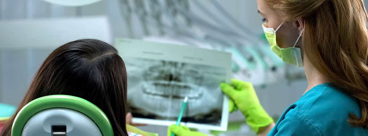 Prevención de la enfermedad periodontal: odontólogo enseñando una radioggrafía de la boca su pacien te