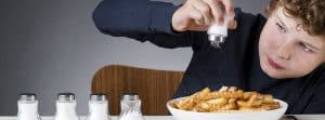 ¿Cómo reducir el consumo de sal en los niños?: niño echando sal en las patatas fritas y varios saleros encima de la mesa